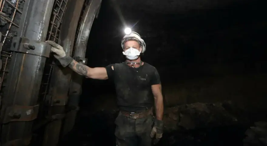 Górnik w kasku z lampką na głowie i masce ochronnej stoi w kopalni. To trudny, ale ważny zawód.