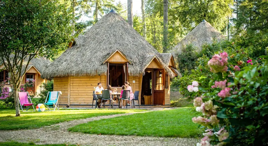Famille profitant d'un repas en terrasse devant leur chalet en chaume, parfait pour des vacances scolaires en Bretagne.