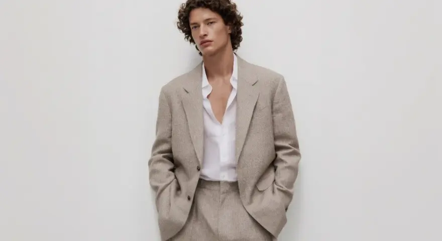 Uomo con capelli ricci indossa un completo beige, incarnando l'eleganza discreta dell'old money significato.