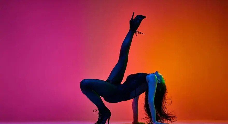 Tancerka w czarnym body i szpilkach wykonuje akrobatyczną figurę na tle gradientu różu i pomarańczy. High heels co to? To buty, które dodają pewności siebie.
