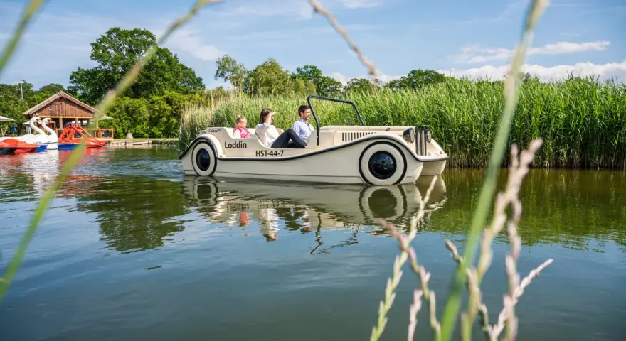 Familie genießt eine Fahrt mit einem Auto-Boot von Kiki's Bootsverleih auf einem ruhigen See, umgeben von üppigem Grün.