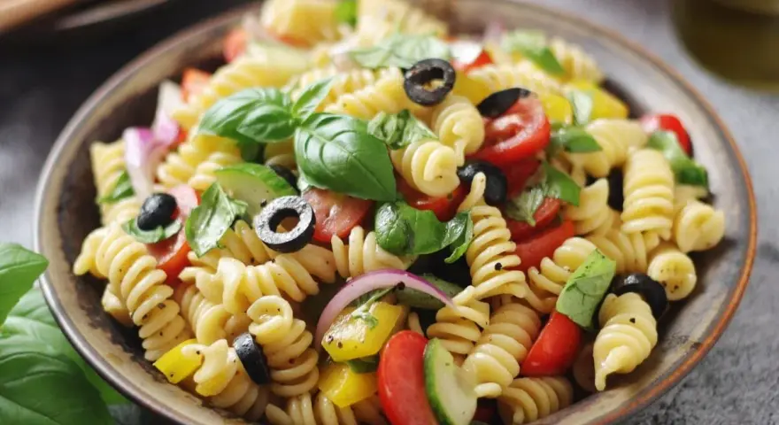Un'insalata di pasta fredda sfiziosa con fusilli, pomodorini, olive nere, cetrioli, cipolla rossa e basilico fresco.