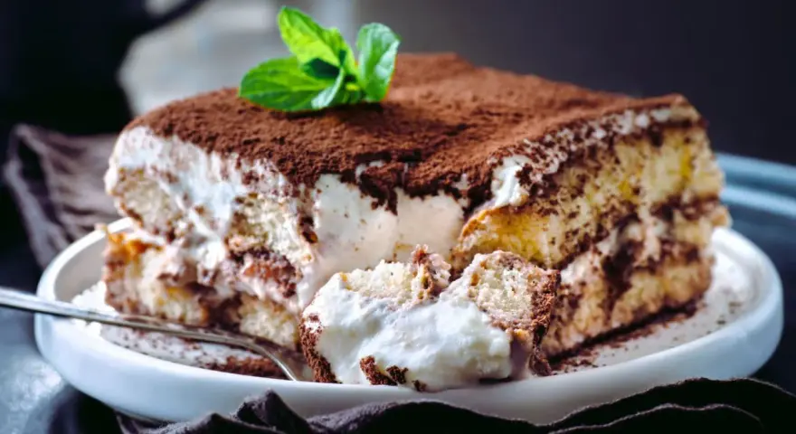 Tiramisú cremoso cubierto de cacao y decorado con menta.