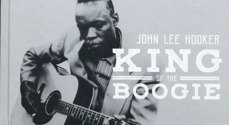 John Lee Hooker, King of the Boogie, spielt Gitarre. Sein Blick ist konzentriert, während seine Finger über die Saiten gleiten.