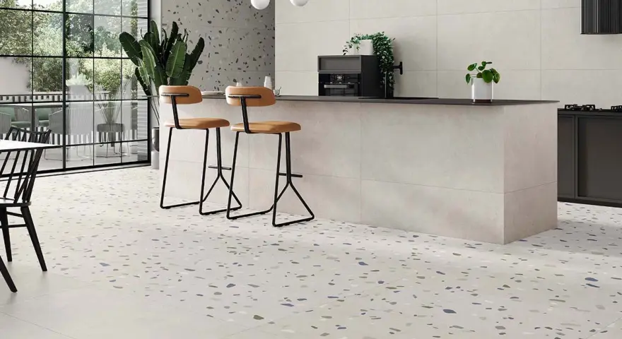 Suelos para cocinas blancas con diseño de terrazo moteado, isla central con taburetes y grandes ventanales.