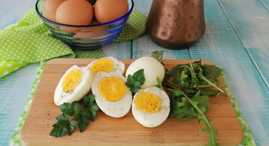 Uova sode in friggitrice ad aria, tagliate a metà, su tagliere con rucola e prezzemolo. Un modo sano e veloce per preparare le uova.