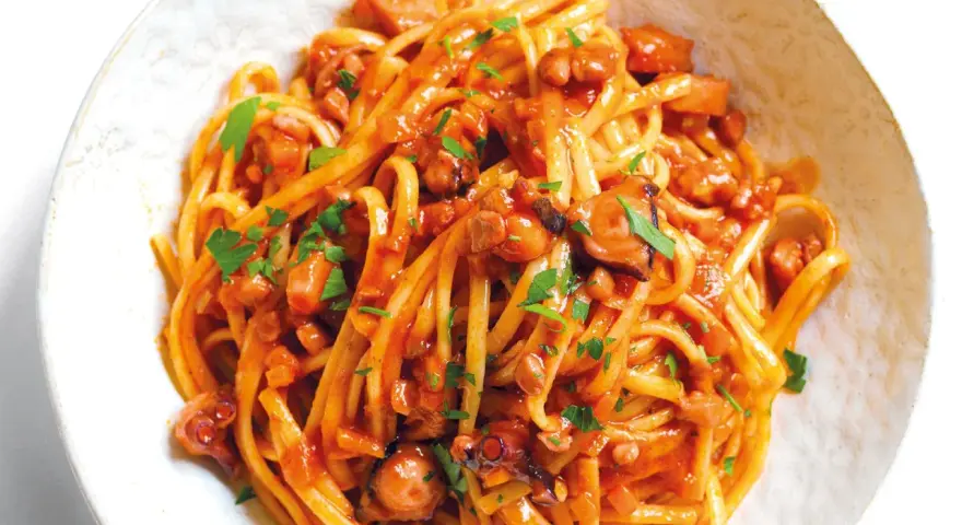 Linguine al ragù di pesce, un piatto saporito con polpo e pomodoro, guarnito con prezzemolo fresco.