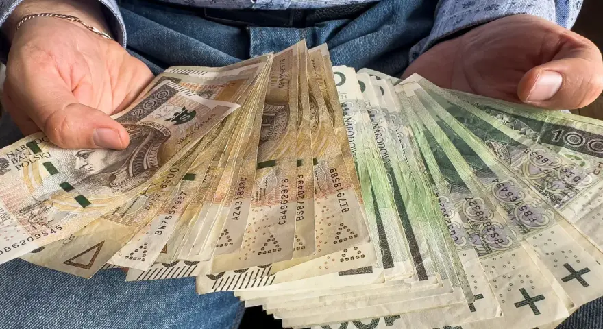 Ręce trzymające stos banknotów, w tym 1000 plus złotych. Widać portret Kopernika na jednym z banknotów.