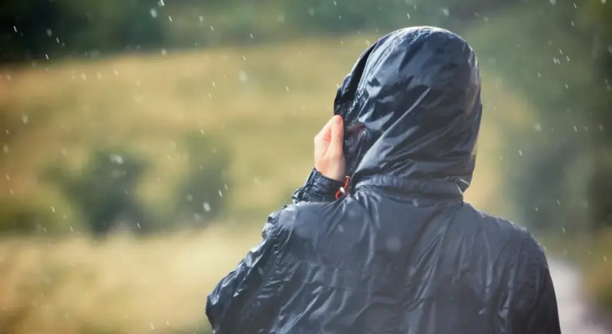 Person im Regen, die Kapuze einer Jacke mit PU-Beschichtung festhält.