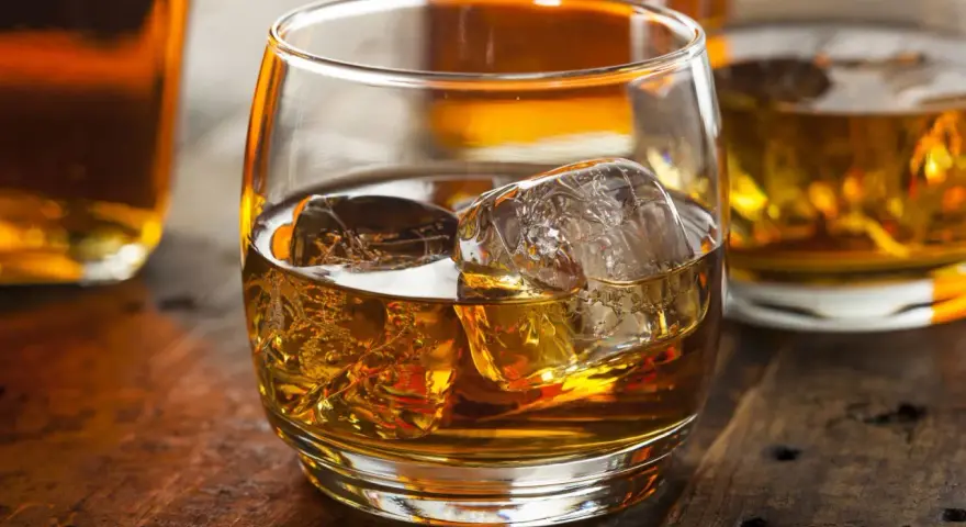 Szklanka złocistego trunku z lodem, obok butelki. Dylemat: whisky szkocka czy irlandzka?