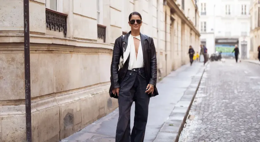 Mujer con gafas de sol y chaqueta de cuero, luciendo un elegante pantalón flare que es tendencia.