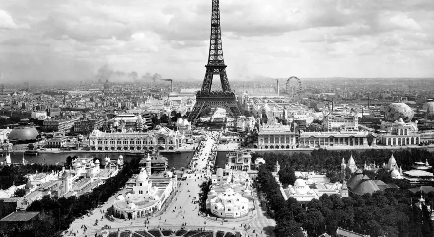 Vista panorámica del **Champ de Mars** con la Torre Eiffel dominando el paisaje, rodeada de pabellones y una noria.
