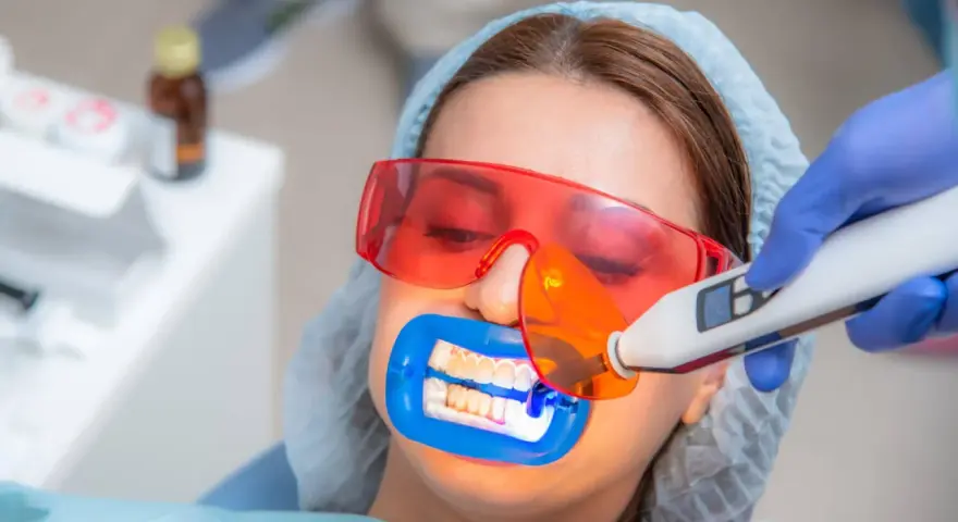 Kobieta przechodzi zabieg wybielania zębów u dentysty. Specjalista używa lampy aktywującej żel wybielający.