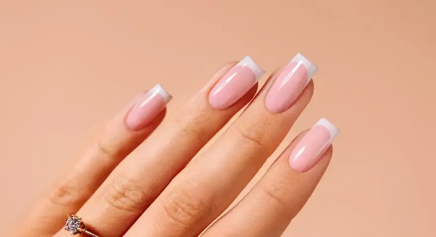 Dłonie z idealnym manicure french na paznokciach. Delikatny róż i biel tworzą klasyczny french na paznokciach, podkreślony subtelnym pierścionkiem.