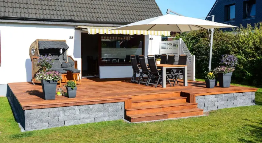 Eine 30 qm Terrasse gestalten: Holzdeck mit Sitzmöbeln, Esstisch, Sonnenschirm und Blumen. Perfekt für entspannte Stunden im Freien.