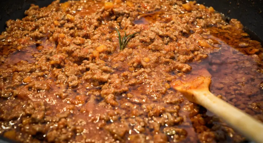 Un saporito ragù di lepre cuoce lentamente in padella, con un rametto di rosmarino che profuma l'aria.
