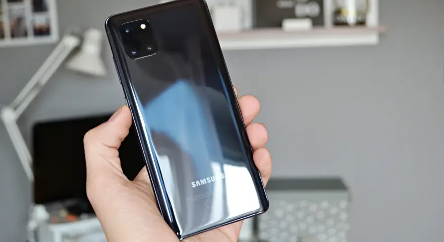 Dłoń trzyma błyszczący, czarny telefon Samsung A81 z modułem aparatów.