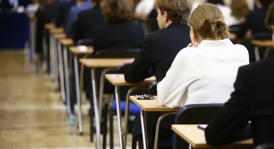 Uczniowie siedzą w rzędach przy ławkach, skupieni na rozwiązywaniu pytań maturalnych.