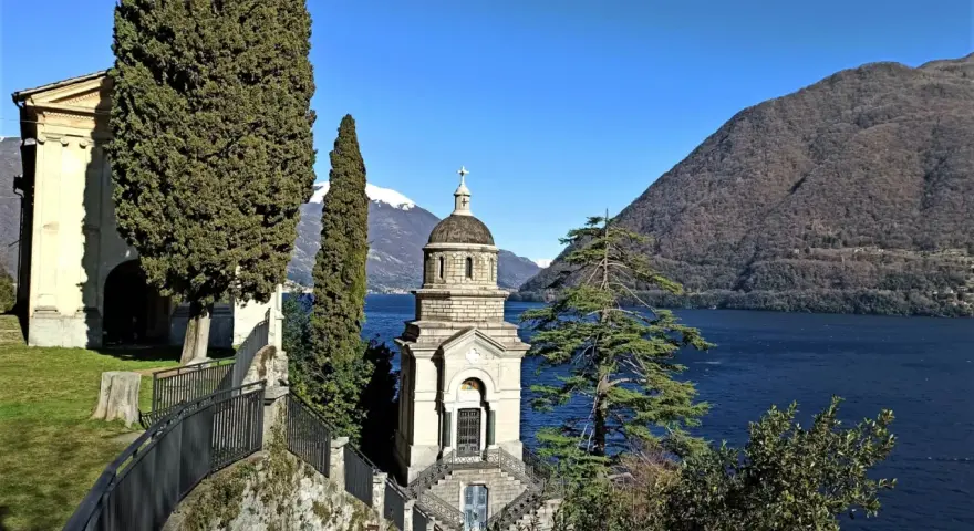 Un suggestivo lago con una piccola chiesa in mezzo, incorniciata da cipressi e montagne innevate.