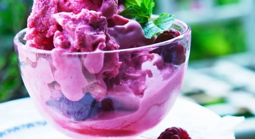 Himbeereis in einer Glasschale, frisch aus der Eismaschine, garniert mit Minze und ganzen Himbeeren.