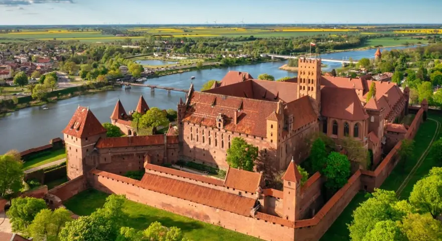 Malbork zamek krzyżacki, potężna twierdza z cegły, góruje nad rzeką Nogat. Otoczony murami, z wieżami i dziedzińcami, zaprasza do odkrywania historii.