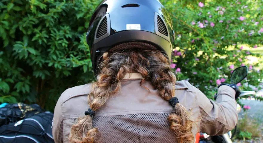 Donna con casco nero e capelli raccolti in due trecce, pronta a legare il casco alla moto.