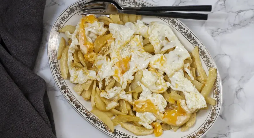 Plato de patatas fritas cubiertas con huevos rotos, con las yemas aún líquidas. Un clásico reconfortante.