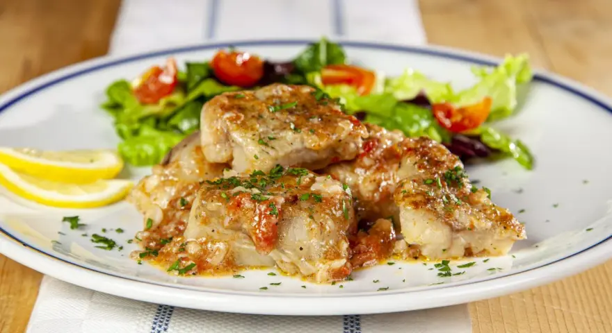 Deliziosa coda di rospo in umido con pomodoro e prezzemolo, servita con insalata fresca e spicchi di limone.