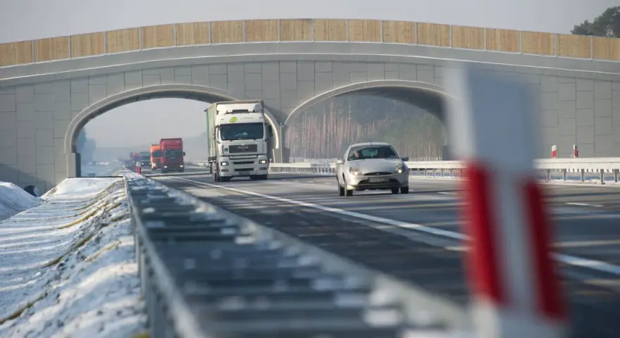 Autostrada A2 z mostem nad jezdnią, jadące samochody i ciężarówki w zimowej scenerii.