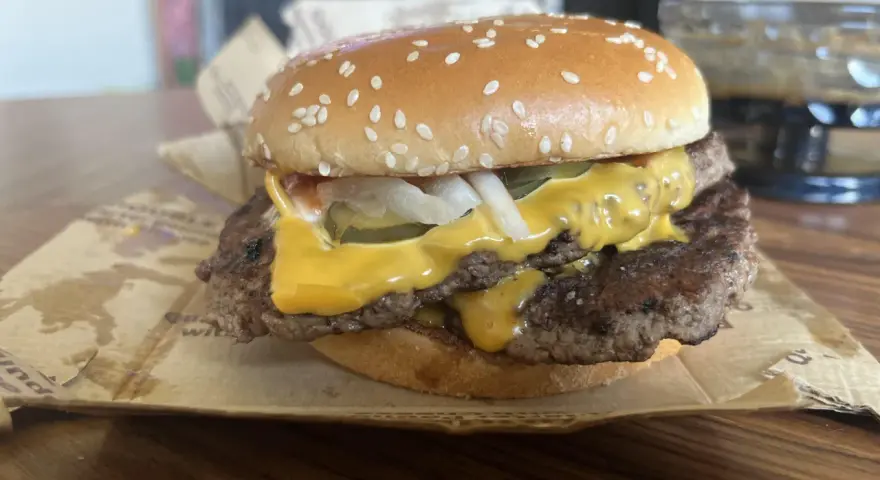 Podwójny cheeseburger z roztopionym serem, piklami i cebulą na bułce z sezamem.