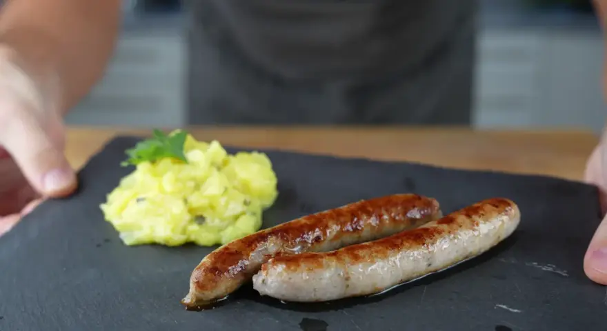 Zwei goldbraune Bratwürste mit Kartoffelsalat, perfekt für alle, die Bratwurst selber machen wollen.