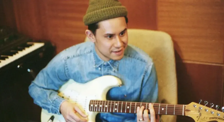 Frank Dukes w zielonej czapce i dżinsowej koszuli gra na gitarze Fender Stratocaster w studiu.