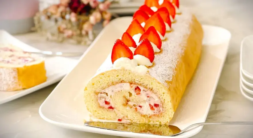 Ein köstliches Biskuitrolle Rezept mit frischen Erdbeeren und Sahne, bestäubt mit Puderzucker.