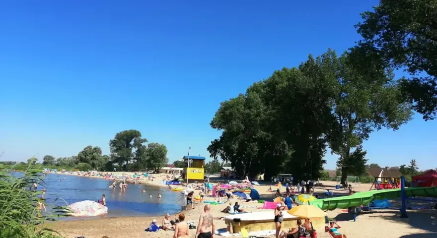 Słoneczny dzień na plaży, ludzie odpoczywają nad wodą. Zastanawiasz się, ile kilometrów jest ze Szczecina nad morze? To idealne miejsce na relaks przed podróżą.