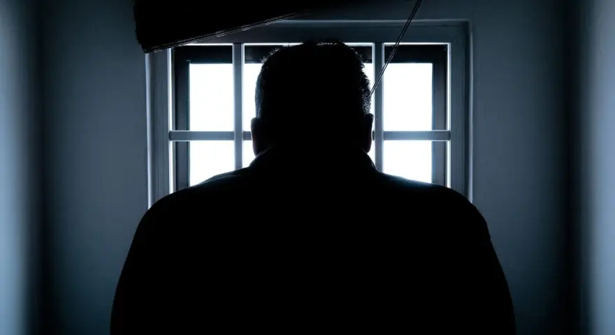Sylwetka mężczyzny wpatrująca się w okratowane okno. Czekam na dzień, gdy dozór policyjny kiedy się kończy i zobaczę wolność.