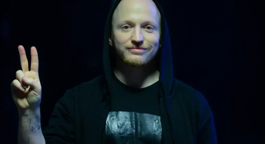 Wojtek Urbański w czarnej bluzie z kapturem pokazuje znak pokoju.