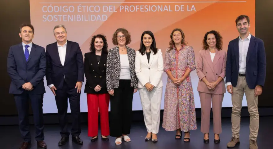 Presentación del código de ética de una empresa. Un grupo de siete profesionales posa en un escenario con un fondo naranja y blanco.