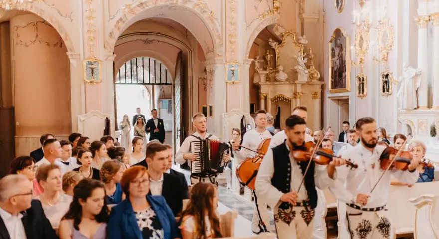 Muzycy w strojach ludowych zapewniają oprawę muzyczną ślubu w kościele. Grają na skrzypcach i akordeonie.