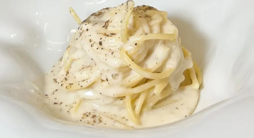 Un piatto di spaghetti cremosi, conditi con un'abbondante dose di cacio e pepe, cosparsi di pepe nero macinato.