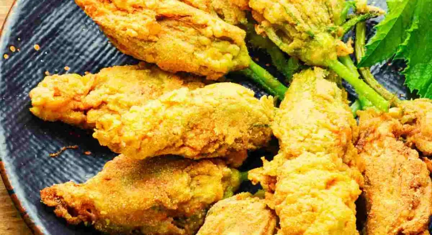 Fiori di zucca ripieni dorati e croccanti, serviti su un piatto blu scuro.