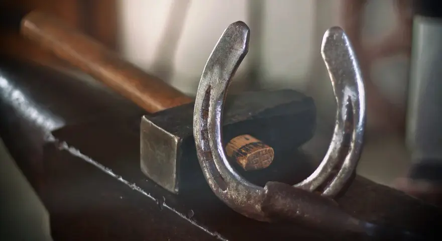 Un fer à cheval usé repose sur une enclume, à côté d'un marteau. L'artisanat du maréchal-ferrant est palpable.