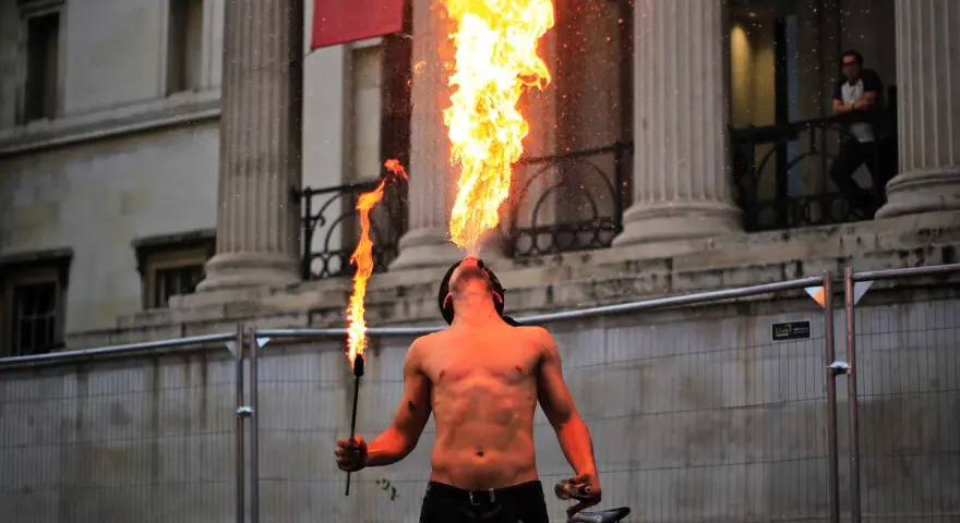 Feuerspucker bläst eine Flamme, während er eine Fackel hält. Der Mann brennt Vodka und zeigt seine Kunst vor einer beeindruckenden Säulenarchitektur.