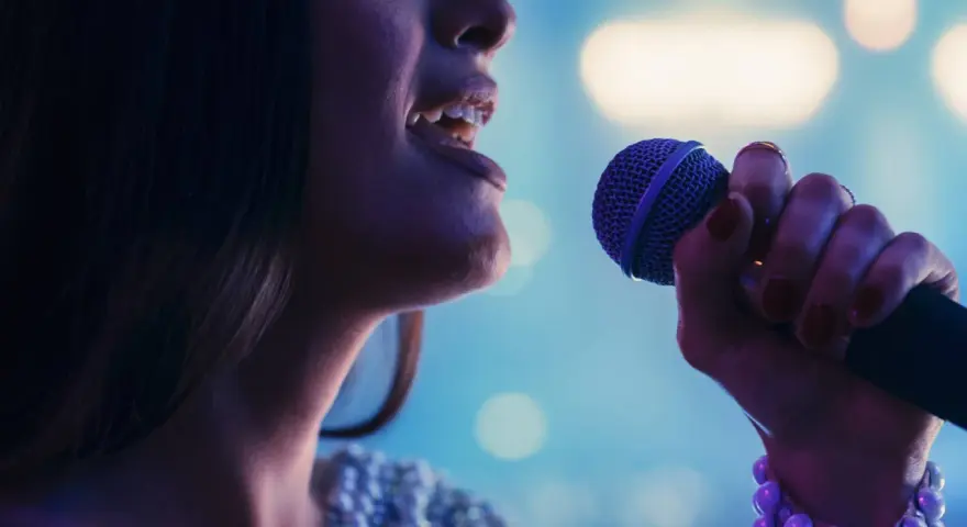 Kobieta śpiewa do mikrofonu. Czy to playback? Wokalistka z błyszczącą suknią i fioletowym mikrofonem.