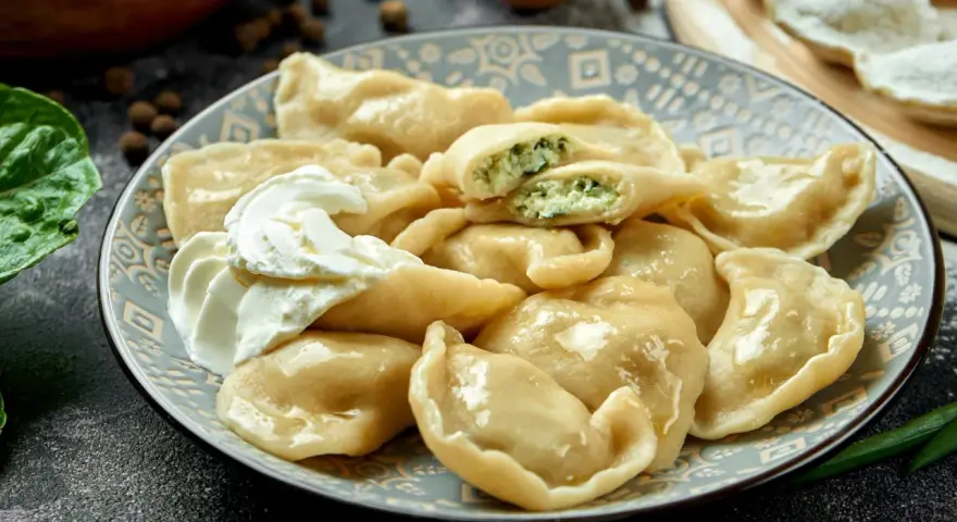 Talerz pierogów ze szpinakiem i twarogiem, z kleksem śmietany.