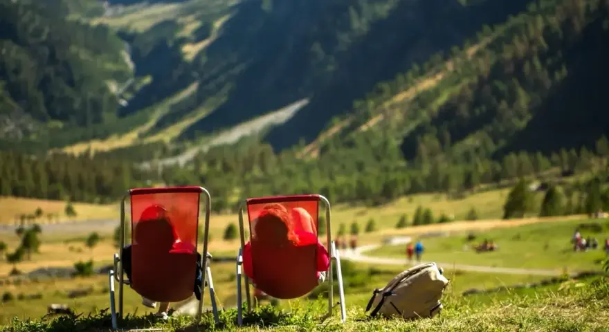 Dwie osoby w czerwonych leżakach podziwiają widok na Alpy w Austrii. Idealne miejsce na camping.