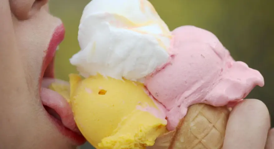 Eiscreme-Liebhaberin schleckt an einem Eis mit drei Kugeln. Die richtige guarkernmehl dosierung macht das Eis cremig.