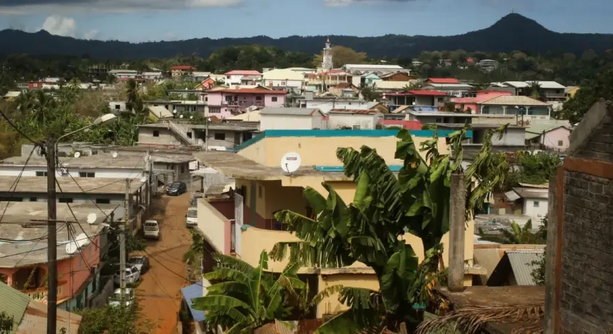 Vue d'une ville aux Comores, Mayotte, avec des maisons colorées, des bananiers et une montagne en arrière-plan.