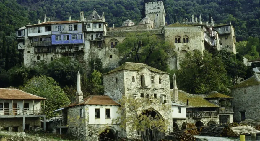 Kamienne budynki klasztorne na zboczu góry Athos, z niebieskim akcentem na jednym z nich.