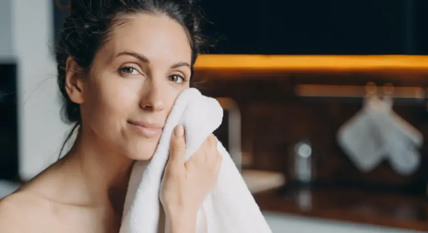 Une femme se sèche le visage avec une serviette. Elle a une peau radieuse, peut-être grâce aux 10 aliments bon pour la peau.