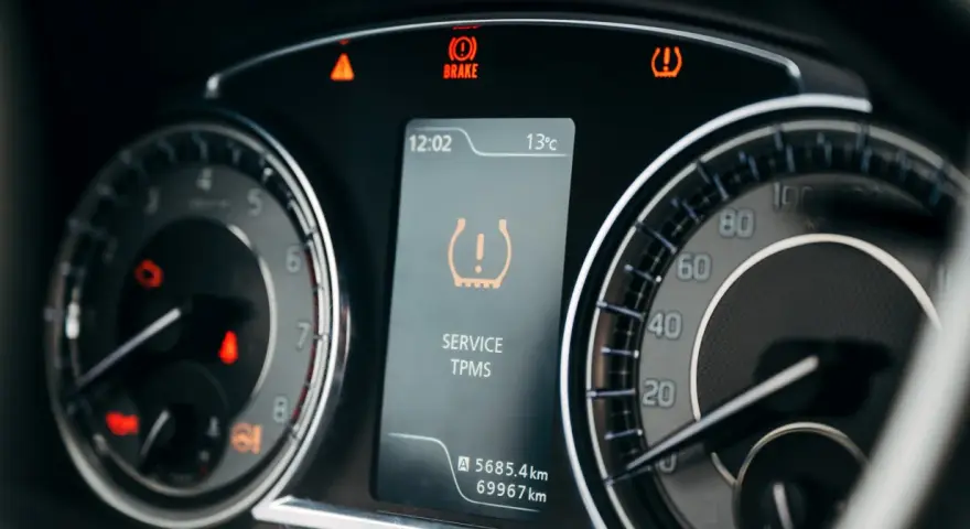 Na desce rozdzielczej świeci się kontrolka niskiego ciśnienia w oponach (TPMS). Obok widać wskaźnik hamulca i ostrzeżenie o temperaturze.